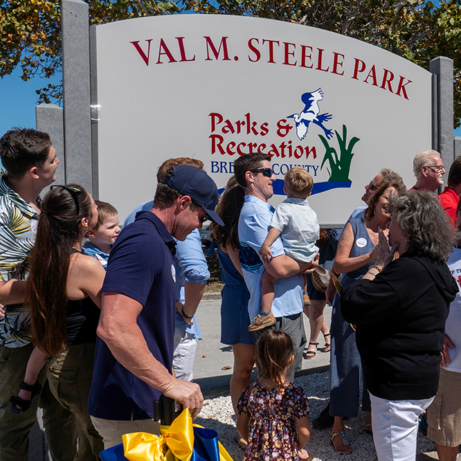 group of family and ceremony attendees gather in front of to witness Val M. Steele Park sign unveiling